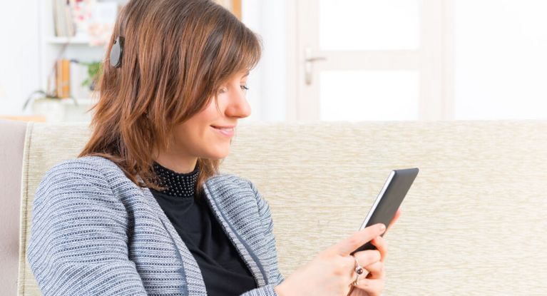 Rehaklinik für Cochela Implantat Frau mit Cochlea Implantat hört Musik am Smartphone