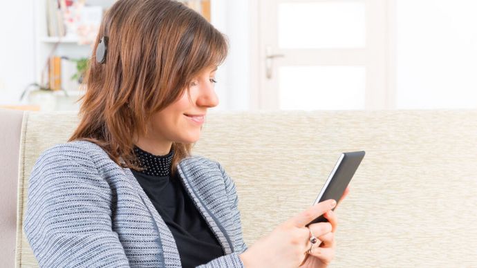 Rehaklinik für Cochela Implantat Frau mit Cochlea Implantat hört Musik am Smartphone